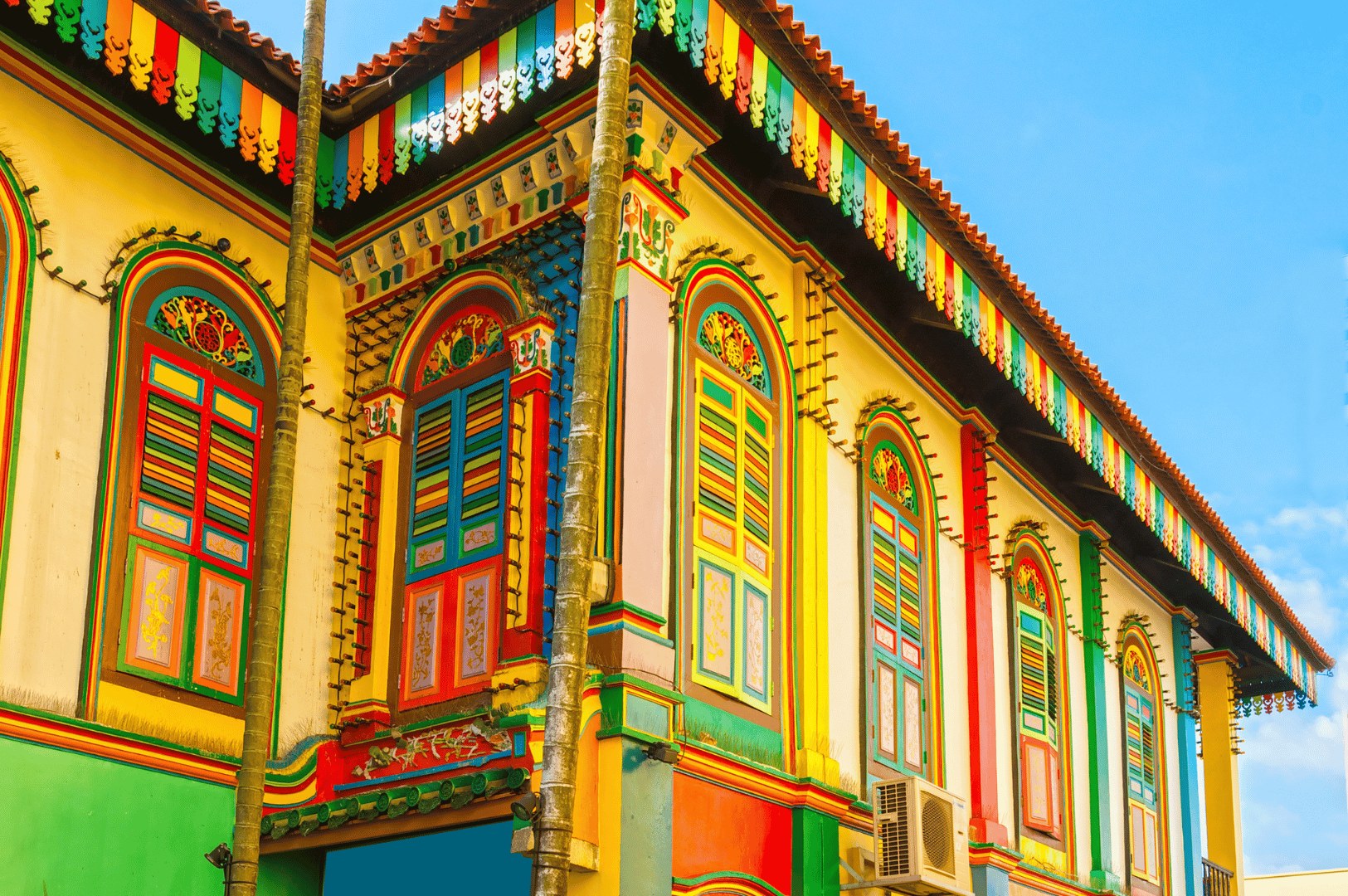 Little-India-Food- (1) Vibrant heritage shophouse in Little India, Singapore, with rainbow-hued wooden shutters and ornate architectural details, evoking the spice-laden warmth and cultural richness of the district—an iconic backdrop for food photography along the Spice Route.