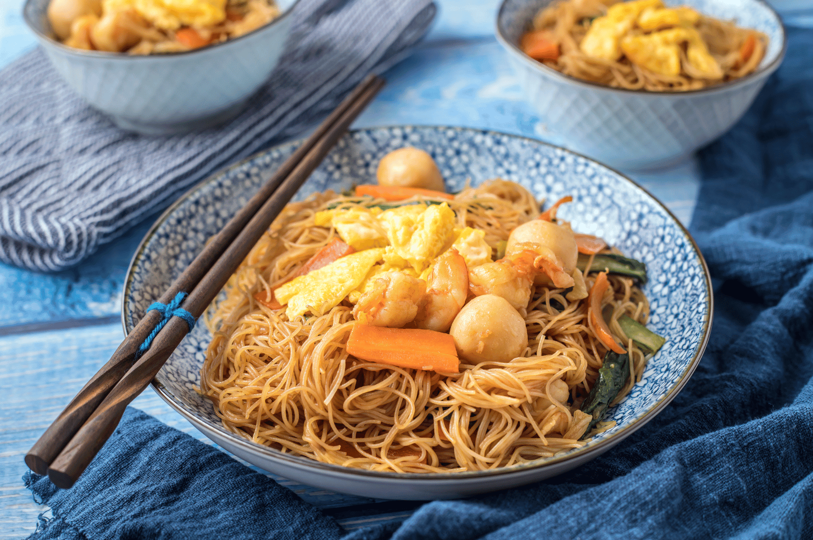 Little-India-Food- (4) Close-up of stir-fried rice noodles with fish balls, scrambled egg, and vegetables in a blue-patterned bowl—an everyday flavor snapshot from Little India’s culinary mosaic. Wooden chopsticks rest on the rim, inviting a taste of the district’s spice-laced street food charm.