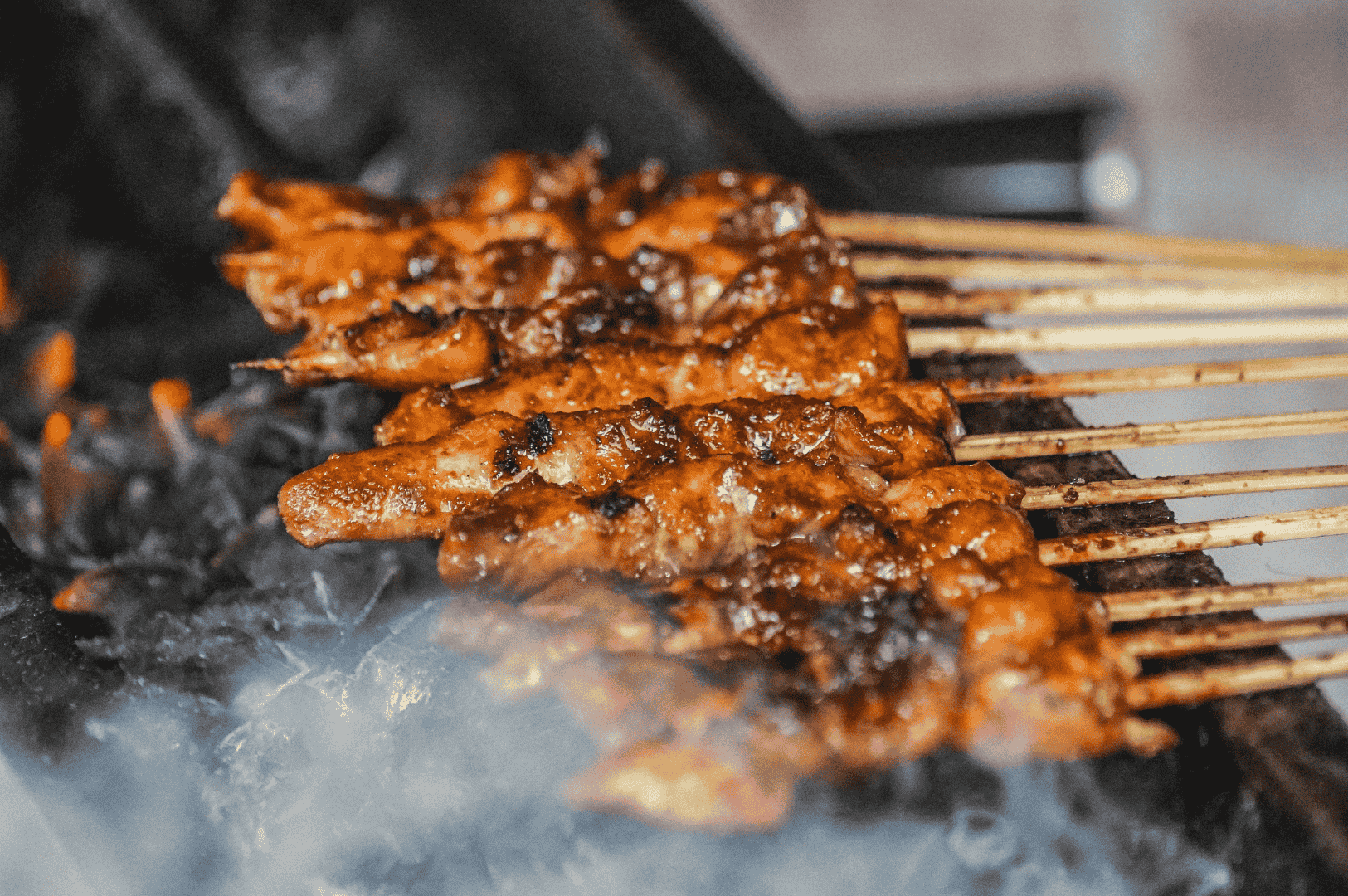 The-Best-Satay-in-Singapore-bts Skewers of well-marinated chicken satay sizzling over a charcoal grill, releasing smoky aroma and showcasing the charred exterior and juicy tenderness that define the best satay in Singapore. This image captures the essence of flame-grilled meat at iconic satay stalls like Chai Ho Satay, Chuan Kee Satay, Shi Xiang Satay, Ah Pui Satay, and Pang's Satay, found in hawker centres such as Lau Pa Sat, Newton Food Centre, and Chinatown Complex Market Food Centre at 335 Smith Street. Whether it’s pork satay, pork belly satay, beef satay, mutton satay, or beef tripe, each satay stick is grilled to perfection and served with rich satay sauce made from peanuts, pineapple puree, and subtle hints of lemongrass, coriander, and cumin. This fiery cooking method delivers succulent flavour, generous portions, and the unmistakable taste of satay in Singapore—sweet, spicy, savoury, and smoky.