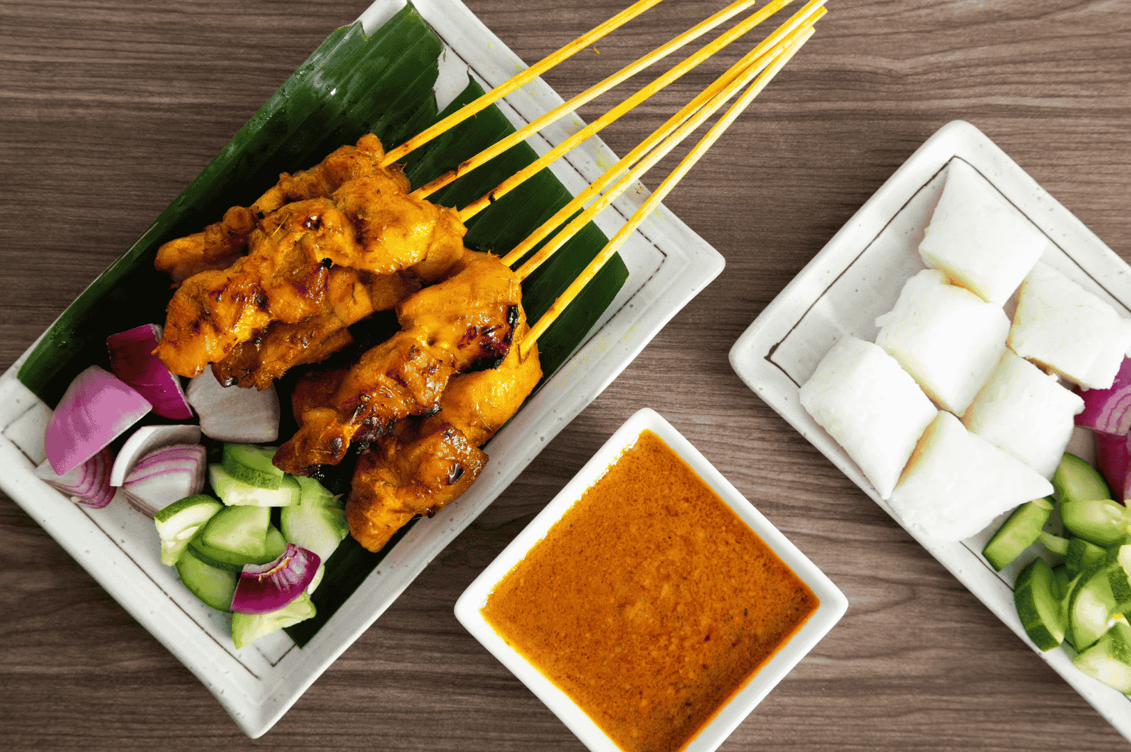 The-Best-Satay-in-Singapore-conclusion Traditional Southeast Asian satay meal featuring grilled chicken satay skewers served on banana leaf-lined plates with rich peanut sauce, ketupat rice cakes, chopped cucumbers, and red onions—capturing the vibrant flavors and presentation of the best satay in Singapore. This dish highlights the juicy, well-marinated meat with a charred exterior, served with satay sauce made from peanuts, pineapple puree, grated pineapple, and subtle hints of lemongrass, coriander, and cumin. Found at iconic satay stalls like Chai Ho Satay, Chuan Kee Satay, Shi Xiang Satay, Ah Pui Satay, Pang's Satay, and Yong Seng Satay across hawker centres such as Lau Pa Sat, Newton Food Centre, and Chinatown Complex Market Food Centre at 335 Smith Street, Singapore’s satay scene offers generous portions of pork satay, pork belly satay, beef satay, mutton satay, lamb, prawns, and beef tripe. This old school satay presentation blends spicy, sweet, and savoury elements, delivering succulent taste and aroma at an affordable price