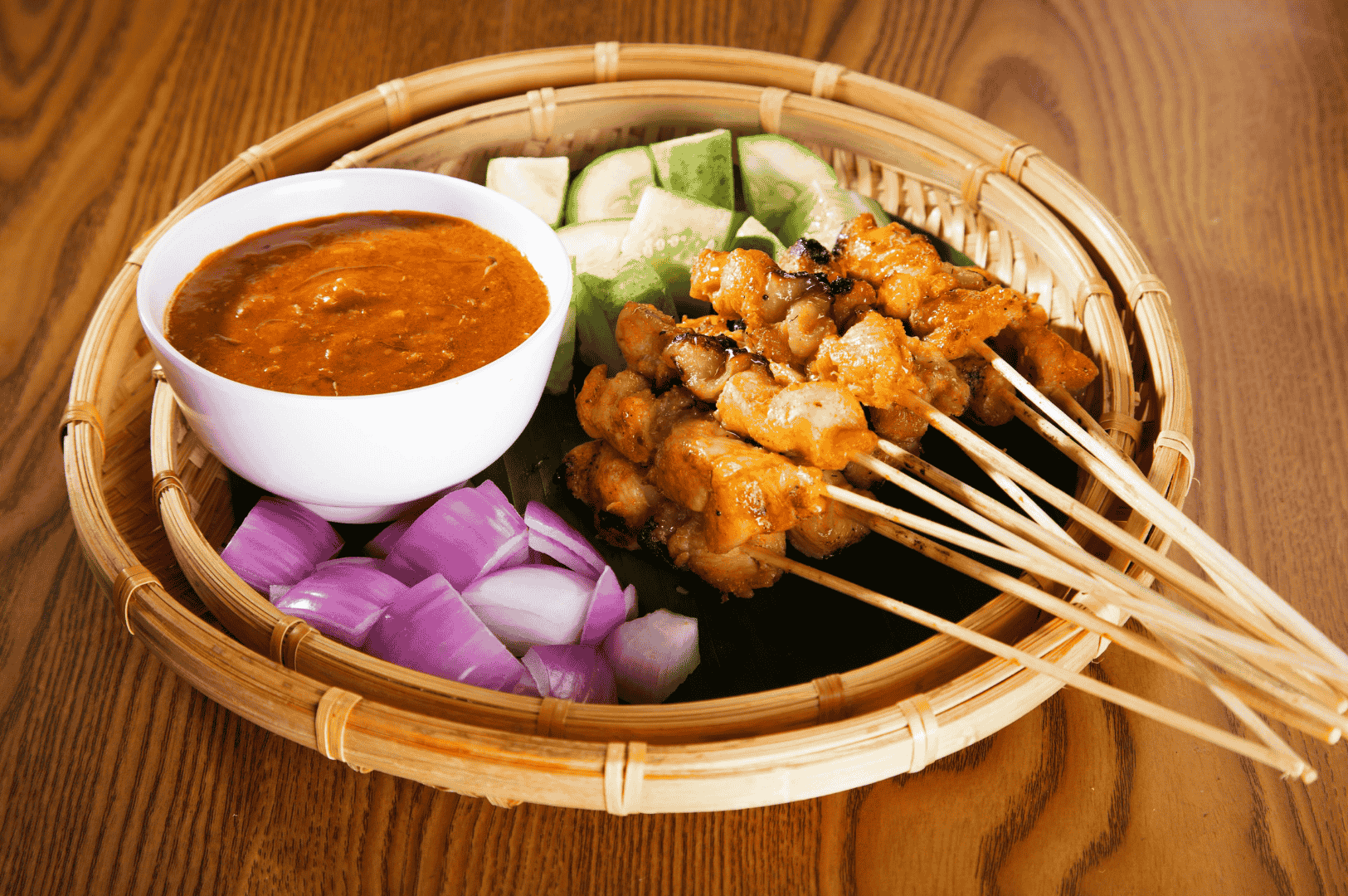 The-Best-Satay-in-Singapore-roots Grilled chicken satay skewers served with thick peanut sauce, chopped onions, and cucumber slices on a rustic bamboo tray—capturing the essence of the best satay in Singapore. This juicy, well-marinated satay features tender meat with a charred exterior and subtle hints of lemongrass, cumin, coriander, and sweet pineapple puree. From pork satay, pork belly satay, beef satay, mutton satay, lamb, prawns, and beef tripe to old school satay and malay style satay, stalls like chai ho satay, chuan kee satay, yong seng satay, shi xiang satay, ah pui satay, pang's satay, and chomp satay at satay street, lau pa sat, newton food centre, and 335 smith street offer generous portions of grilled meat at affordable price. Found in hawker centres like complex market food centre and chinatown complex market food at 335 smith street, satay in Singapore is known for its succulent taste, savoury satay sauce, grated pineapple, sweet aroma, and delicious peanuts. Five sticks of lean meat or oily cuts, well grilled and served with spicy sauce, deliver a flavourful bite that defines the best satay experience at any food centre or stall.