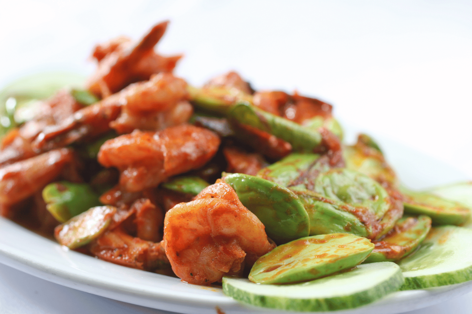 Chinese-Malay-Fusion- (2) Close-up of stir-fried shrimp glazed in spicy sambal sauce, intermingled with vibrant green petai beans and framed by crisp cucumber slices—an aromatic, unapologetically bold dish that captures the rebellious spirit of Chinese-Malay fusion, where Peranakan finesse meets Nyonya fire in Singapore’s culinary underground.