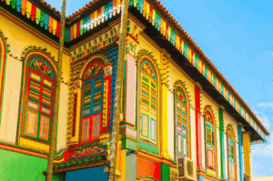 Vibrant heritage shophouse in Little India, Singapore, with rainbow-hued wooden shutters and ornate architectural details, evoking the spice-laden warmth and cultural richness of the district—an iconic backdrop for food photography along the Spice Route.