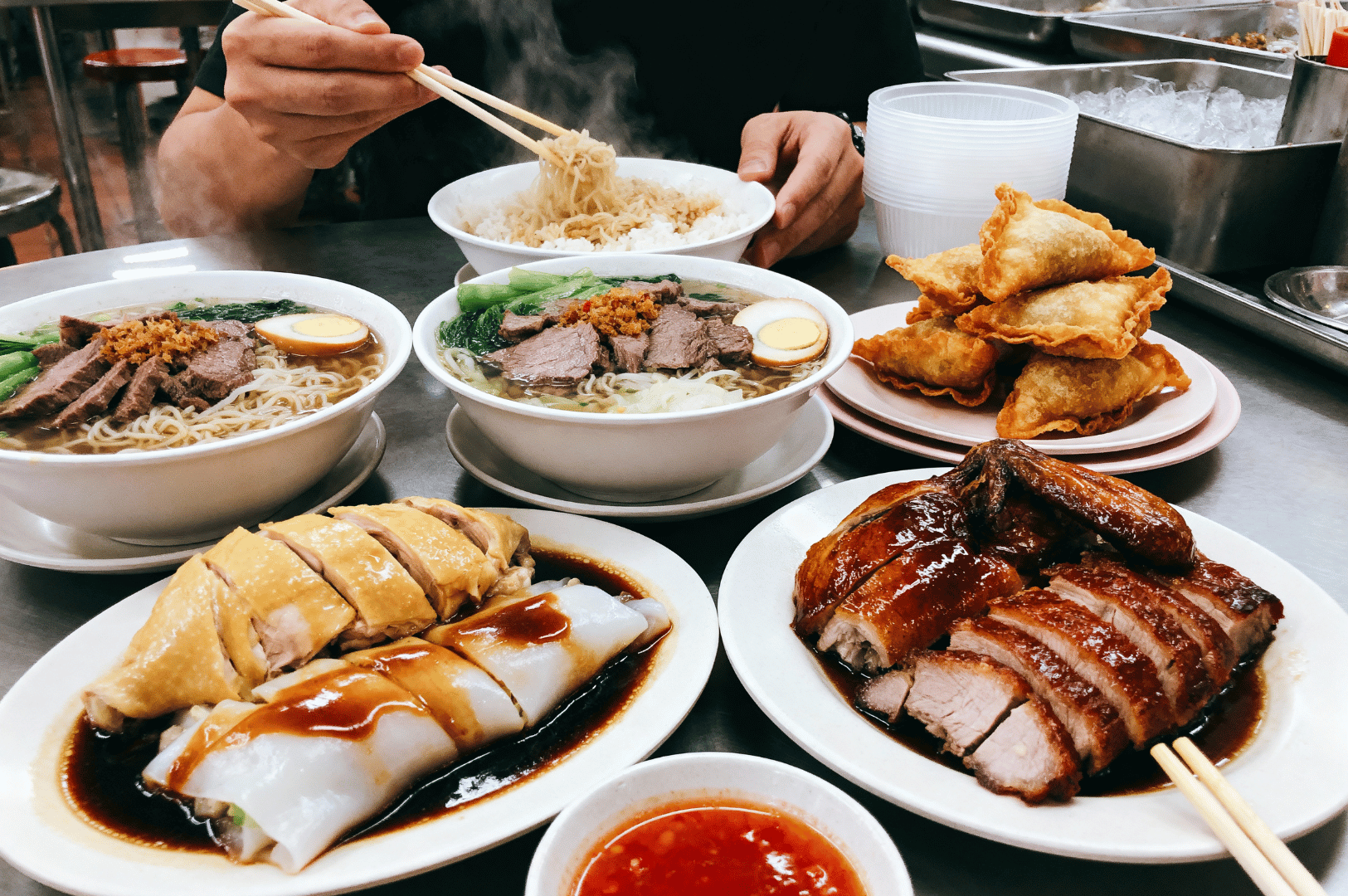 Table spread of Chinese noodle soup, roasted duck, dumplings, and rice rolls at a Singapore Chinatown eatery — highlighting the diversity and richness of Chinese culinary heritage.