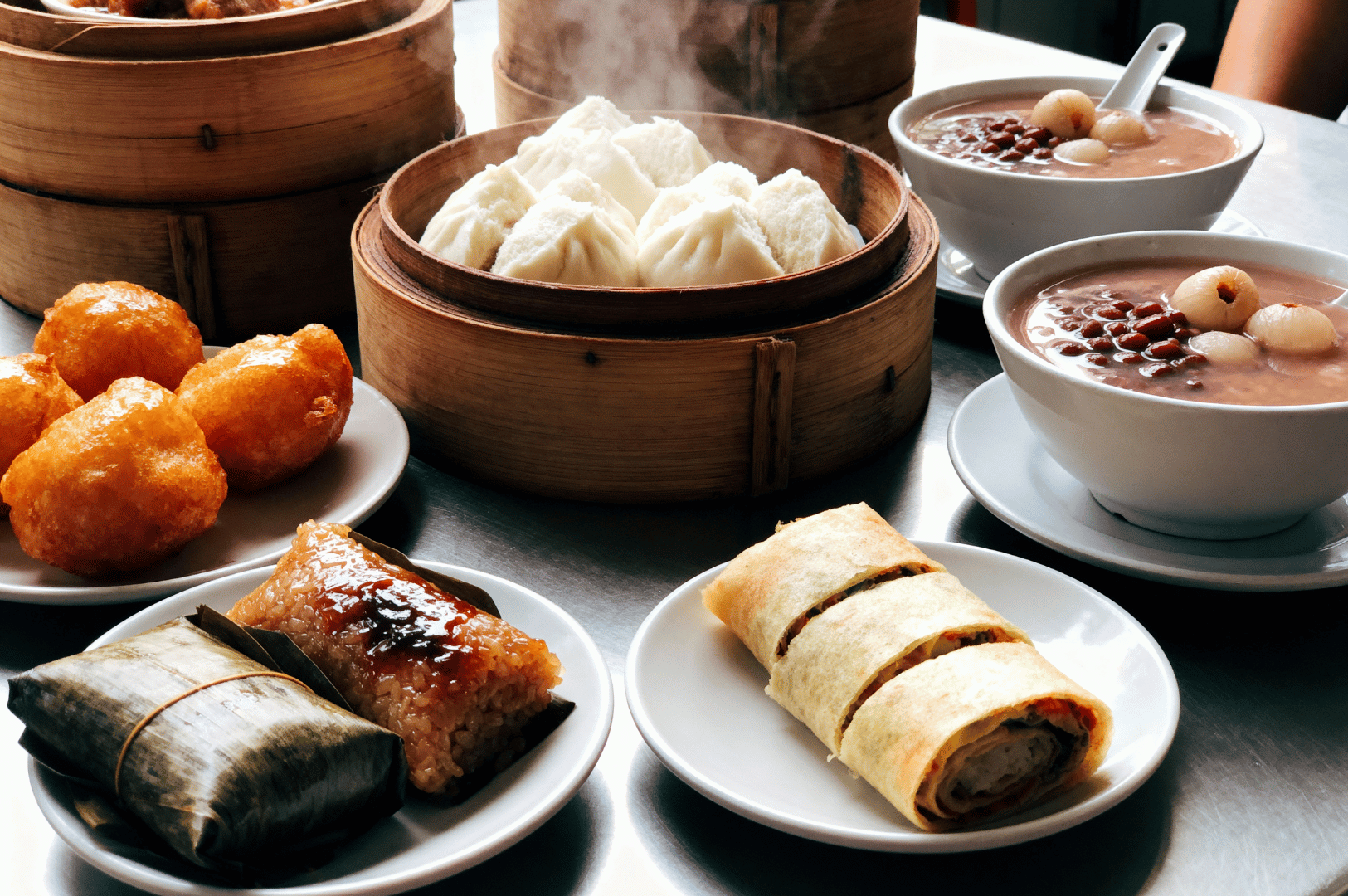 Assorted dim sum dishes at a Singapore Chinatown table, featuring steamed buns, sweet red bean soup, sticky rice dumplings, and golden fried snacks — celebrating the variety of Chinese culinary heritage.