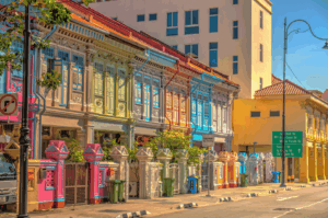 A pastel-hued row of Peranakan shophouses in Katong, Singapore, bursts with architectural charm—ornate wooden shutters, tiled roofs, and decorative moldings echoing colonial and local styles—setting a vibrant stage for the district’s rich street food culture.