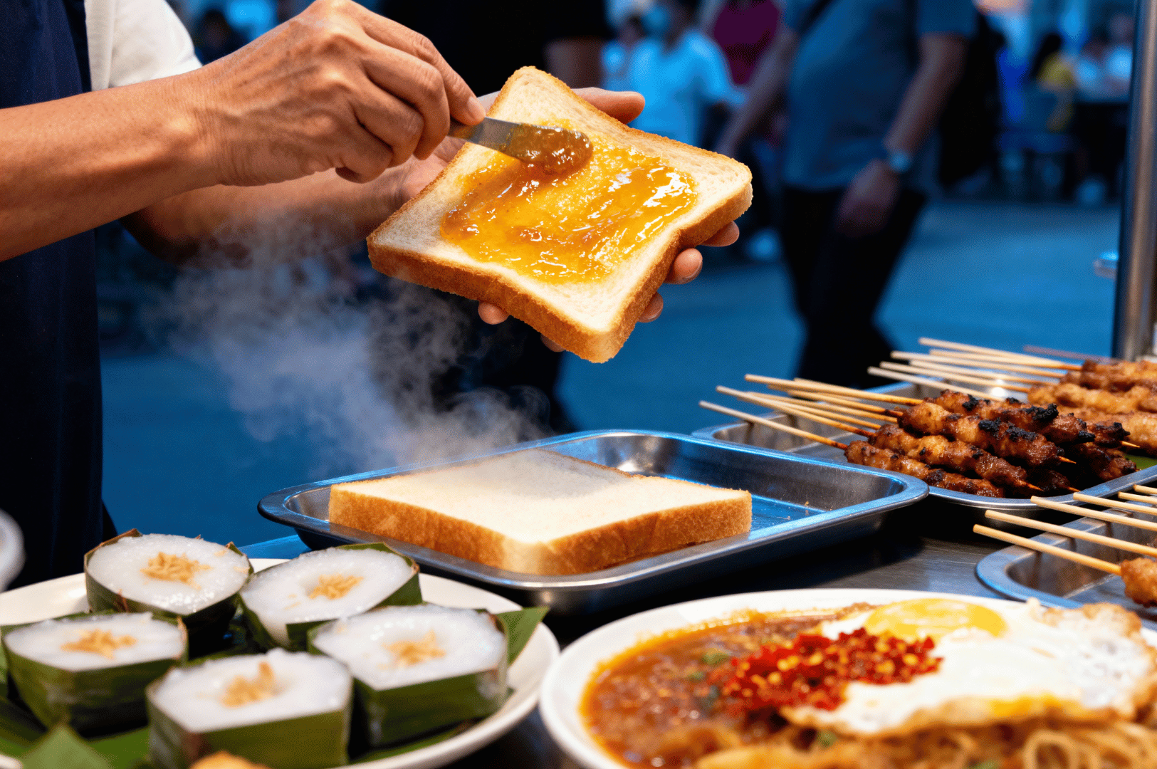 Morning- (3) Close-up of a vendor spreading kaya jam on warm toast at a bustling Singapore street stall, with steaming dishes and satay skewers nearby.