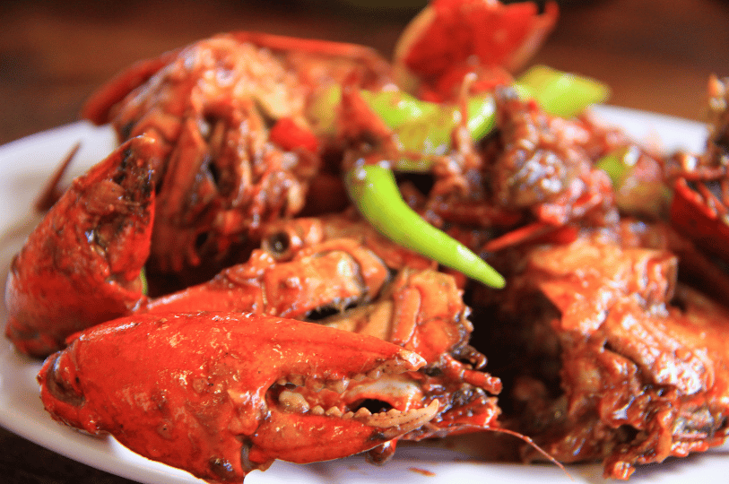 Chili-Crab- (4) A close-up, sensory shot of a cracked crab claw coated in a spicy, textured chili paste and topped with bright green bird's eye chilies.