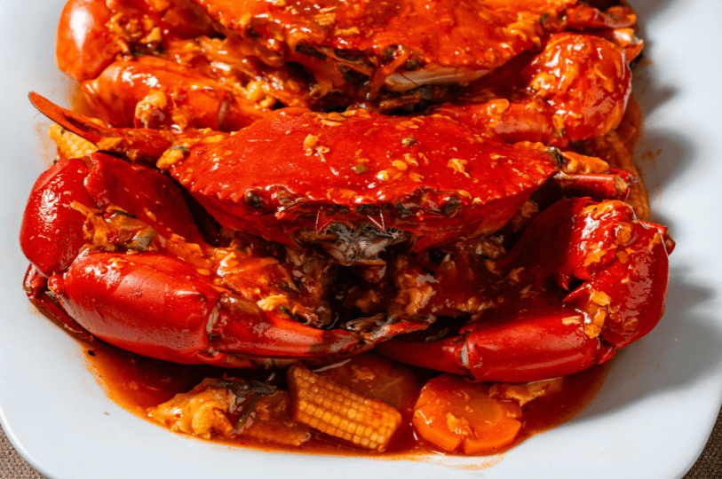 Chili-Crab- (5) A top-down view of two large chili crabs on a platter, showcasing the deep crimson shells and a vibrant orange-red sauce simmered with vegetables.