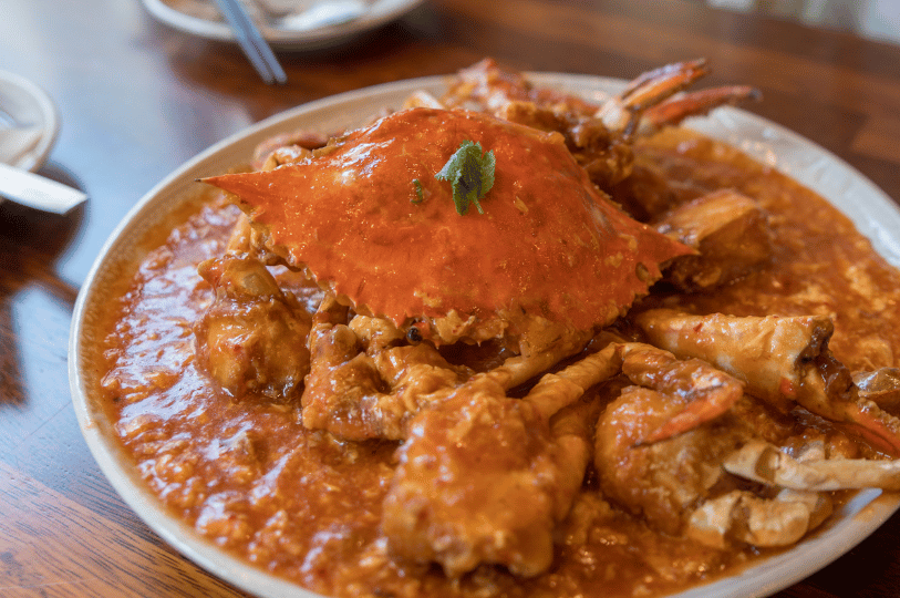 Chili-Crab- (6) A wide-angle shot of a classic Singaporean chili crab in a shallow bowl, featuring a silky, tomato-hued gravy with delicate egg ribbons and a single cilantro leaf garnish.