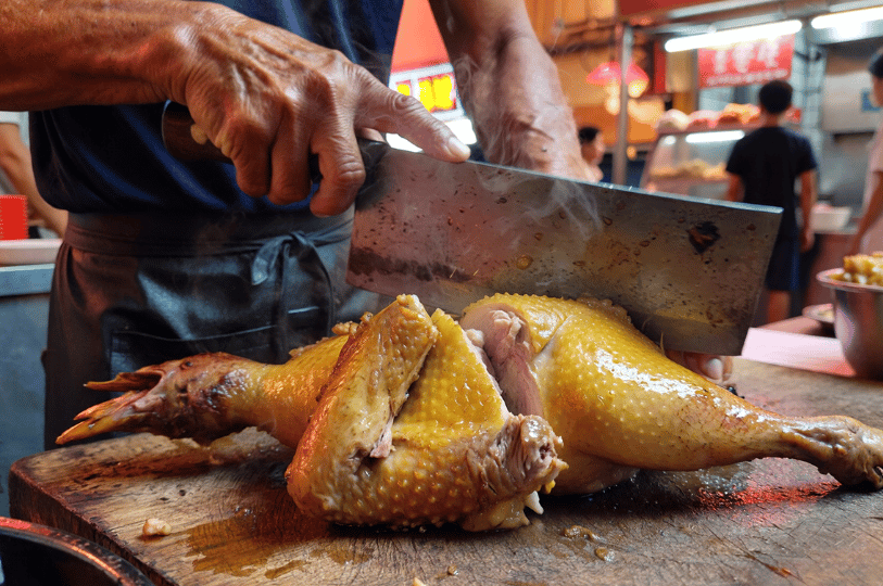 In-Motion- (2) A motion-focused shot of a chef’s hands using a heavy metal cleaver to slice through a roasted chicken on a wooden block, with a slight blur on the blade to emphasize the speed of the strike.