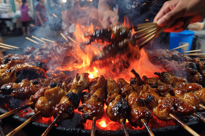In-Motion- (3) A close-up, low-angle shot of chicken satay skewers grilling over an intense open flame, with sparks and smoke rising to convey the heat and energy of street food cooking.