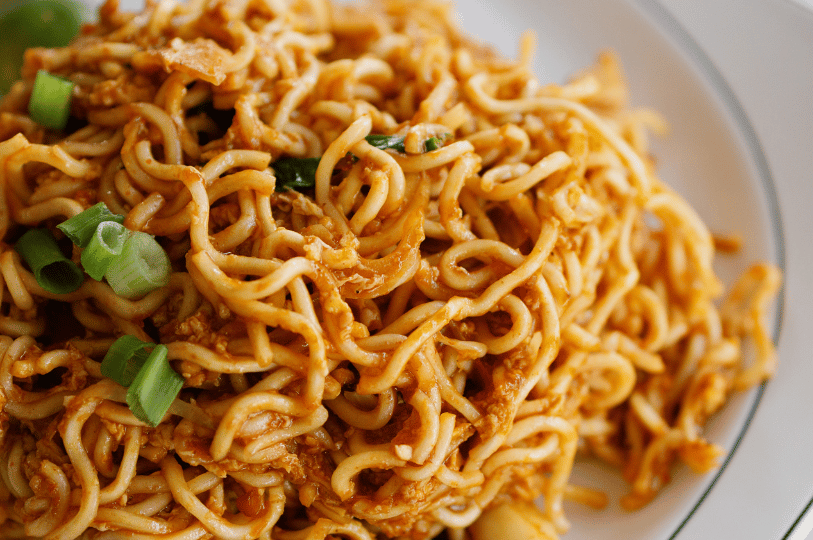 Art-of-the-Tease- (4) A tight detail shot of stir-fried noodles tangled together in a savory, reddish-brown sauce. Freshly chopped scallions provide a pop of color, highlighting the moist, springy texture of the dish.