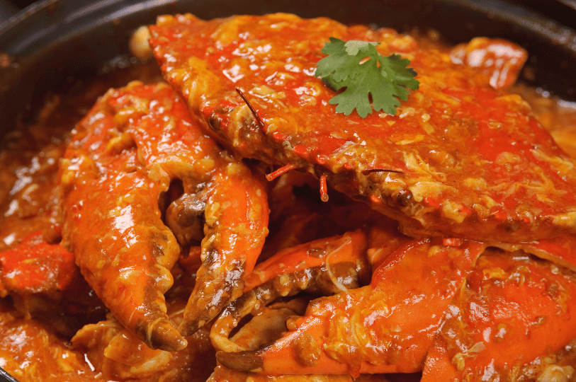 A medium close-up of crab claws and shell partially submerged in a rich, bubbling chili sauce. A single cilantro sprig sits on top, showcasing a shallow depth of field that keeps the focus on the glossy texture of the sauce and shell.