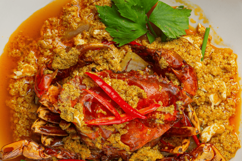 An overhead "flat lay" composition of chili crab, featuring the main shell centered and topped with long red chili slices and celery leaves. The shot emphasizes the texture of the thick, egg-ribboned sauce and the symmetry of the plating.