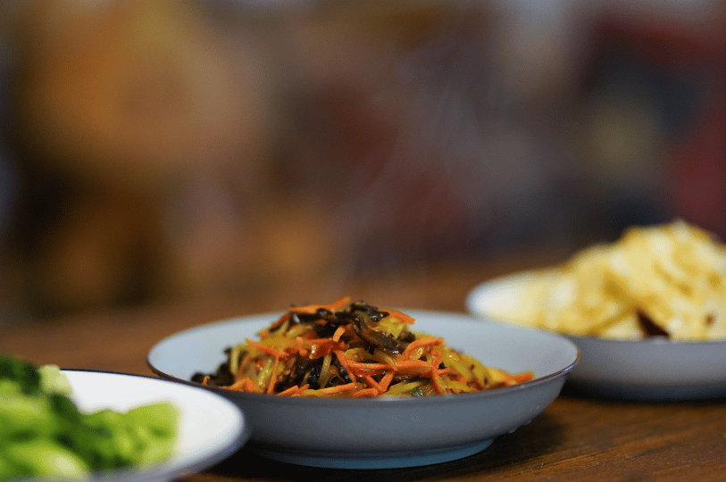 Composition- (3) A shallow depth-of-field shot of a small plate of stir-fried vegetables and wood ear mushrooms utilizing negative space. The sharp focus on the central plate against a heavily blurred background creates a minimalist, "hero" shot of the dish.