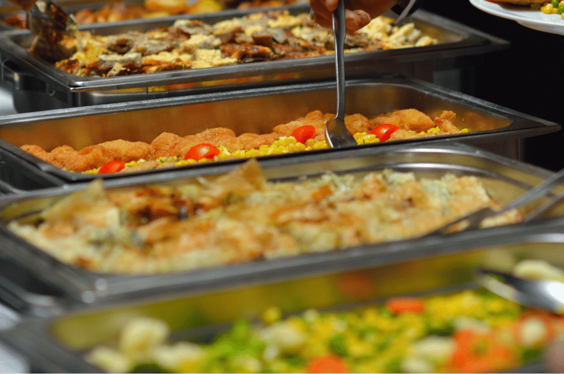 Composition- (4) A side-angle shot of various buffet trays filled with steamed fish and vegetables utilizing leading lines. A serving spoon is partially visible, using a repetitive horizontal pattern of stainless steel trays to create a sense of abundance and depth.