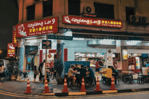 Nighttime street scene outside Geylang Lor 9 Fresh Frog Porridge, with diners at outdoor tables under glowing red signage, capturing the district’s lively, late-night allure and culinary boldness.