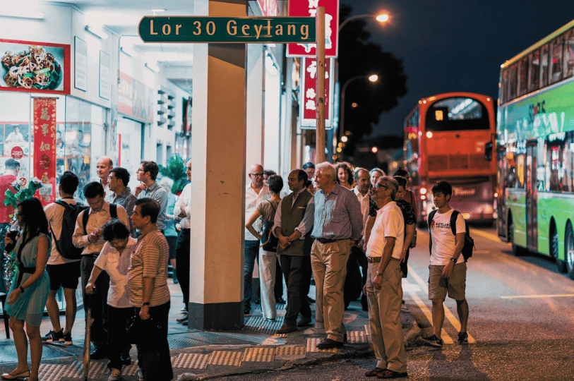 Geylang- (5) Crowd gathered outside a brightly lit restaurant on Lorong 30 Geylang, with double-decker buses passing by—an electric snapshot of the district’s nocturnal pulse, where food, transit, and anticipation collide.