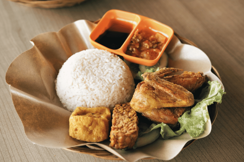 A close-up of traditional Nasi Lemak served on a banana leaf, topped with spicy sambal, crispy ikan bilis (anchovies), roasted peanuts, and a fried egg.