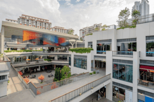 An elevated view of One Holland Village’s modern open-air courtyard, featuring multi-level walkways, contemporary art installations, and integrated green spaces.