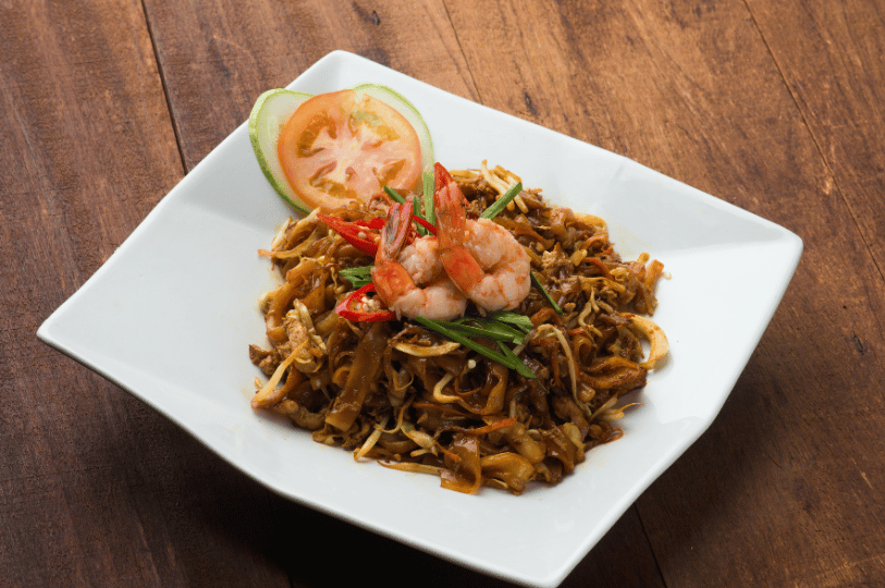 Holland-Village- (3) A vibrant plate of Char Kway Teow topped with succulent prawns and fresh chili, served on a square white plate to highlight traditional local flavors.