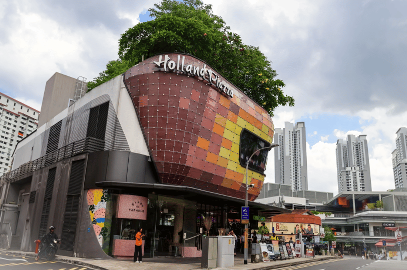 Holland-Village- (4) The iconic Holland Piazza building featuring a modern, curved mosaic facade in warm tones, topped with lush greenery against a backdrop of Singapore’s high-rise apartments.