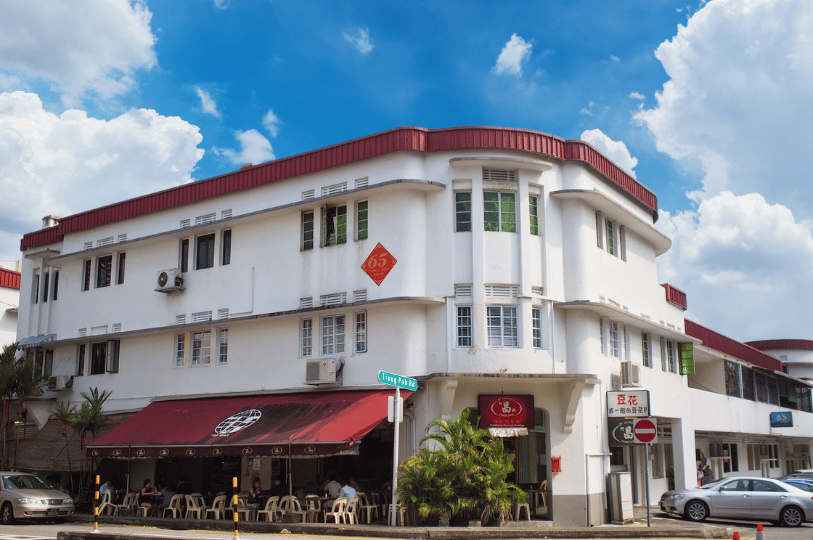 Tiong-Bahru- (2) An architectural shot of a classic Art Deco shophouse in Tiong Bahru under a bright blue sky. The white building features rounded balconies, a red awning for a ground-floor cafe, and iconic Streamline Moderne curves.