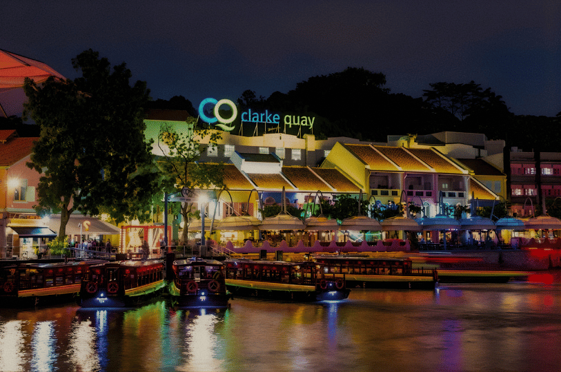 A scenic night view of Clarke Quay’s colorful restored shophouses reflected in the Singapore River, featuring riverside dining and iconic bumboats.