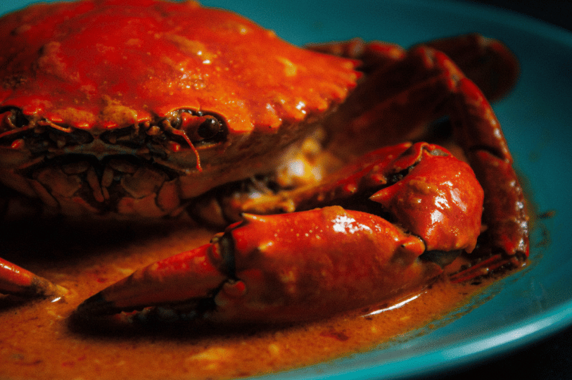 An extreme close-up of Singapore Chili Crab bathed in a rich, glossy red sauce. The image demonstrates split-tone color grading with warm highlights emphasizing the spice and cool shadows adding depth to the crab shell, showcasing a cinematic food photography style.