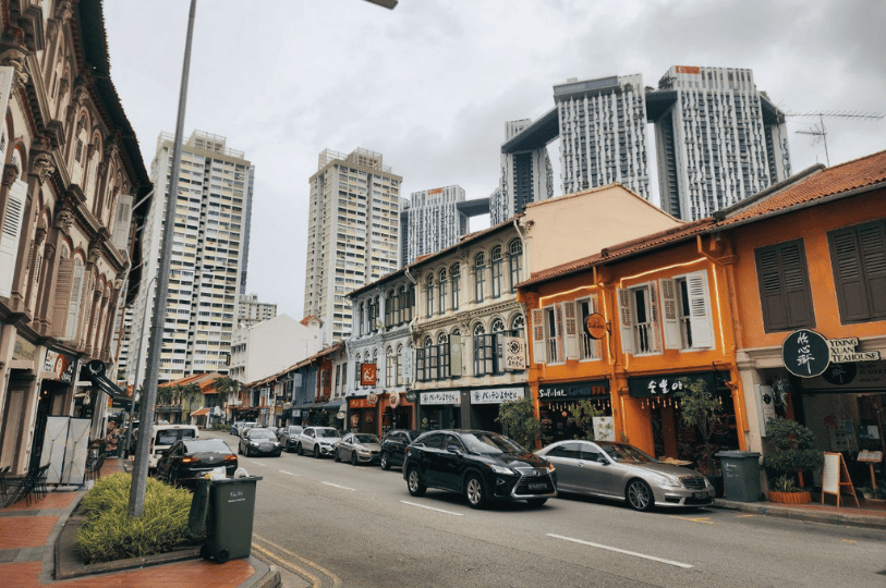 TanjongPagar- (5) A street-level view of Tanjong Pagar Road lined with colorful historic shophouses housing restaurants and teahouses, contrasted by the towering, modern sky-bridge architecture of the Pinnacle@Duxton in the background.