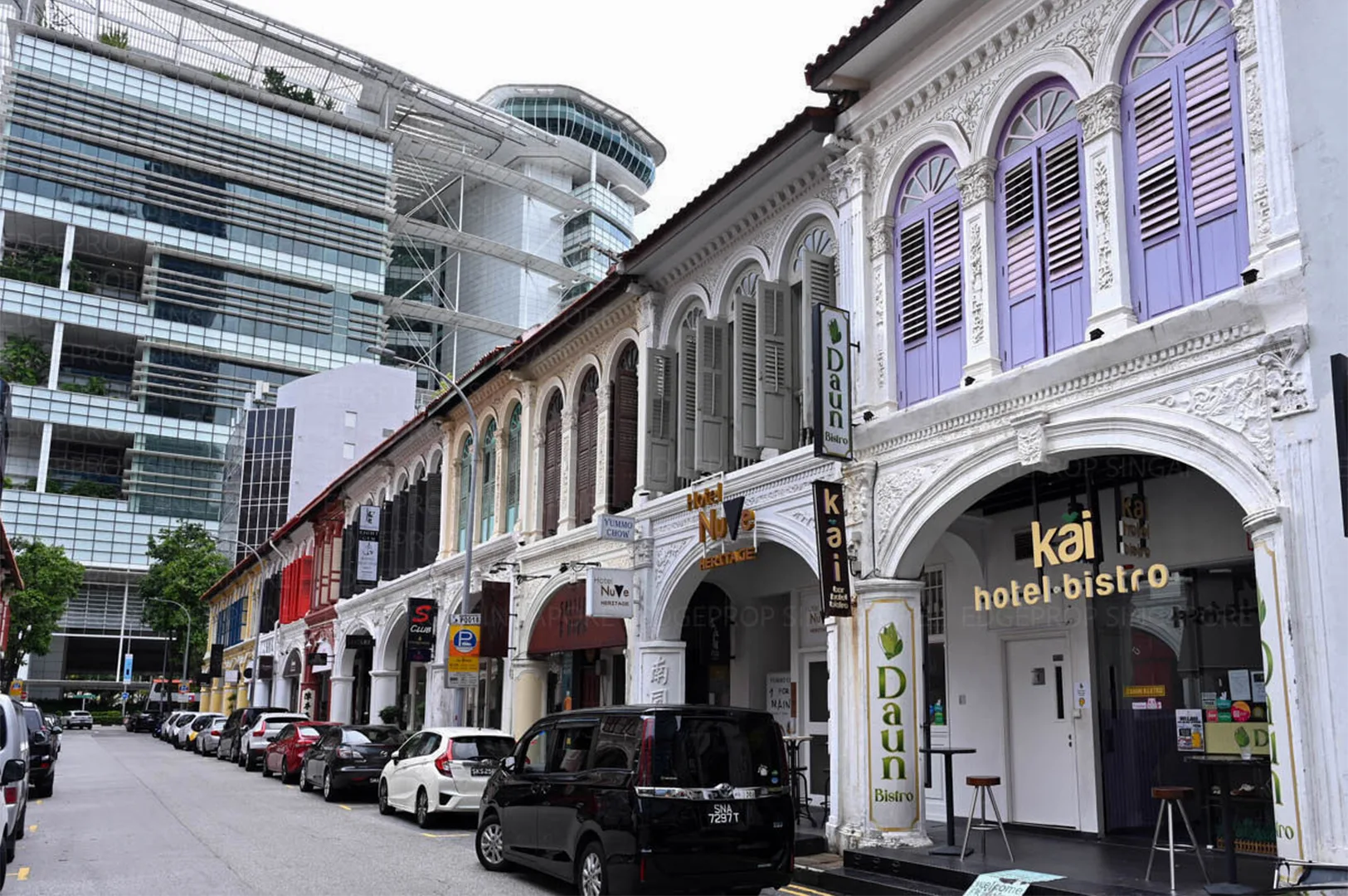 4-purvis-street-heritage-shophouses.webp A row of beautifully restored white and pastel-colored heritage shophouses with arched walkways and parked cars on a quiet Singapore street.
