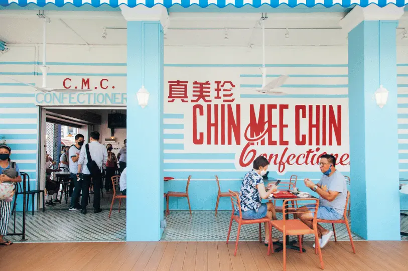 Breakfast-Spots- (2) Bright, naturally lit shot of patrons dining outside the retro Chin Mee Chin Confectionery, framed against a highly photogenic light blue and white striped wall with bold red typography.