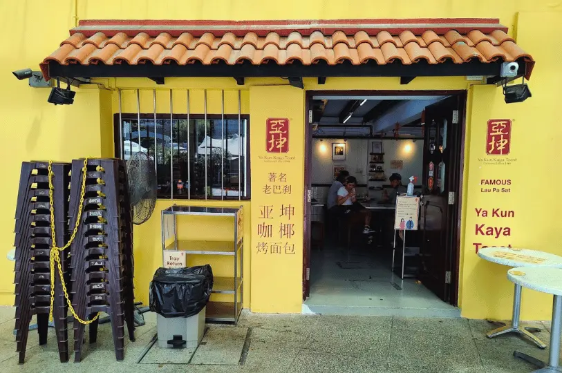 Breakfast-Spots- (4) Straight-on, high-contrast visual of the Ya Kun Kaya Toast outlet, highlighting the vivid yellow exterior walls contrasting with the darker, inviting interior where diners are seated.