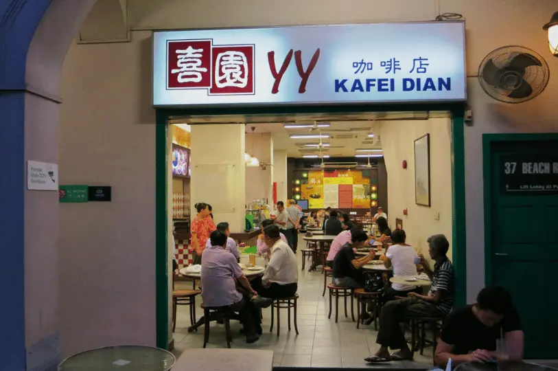 Breakfast-Spots- (7) A glowing, wide-angle shot looking into the open front of YY Kafei Dian, contrasting the dim exterior with the warmly illuminated, bustling interior full of locals enjoying breakfast.