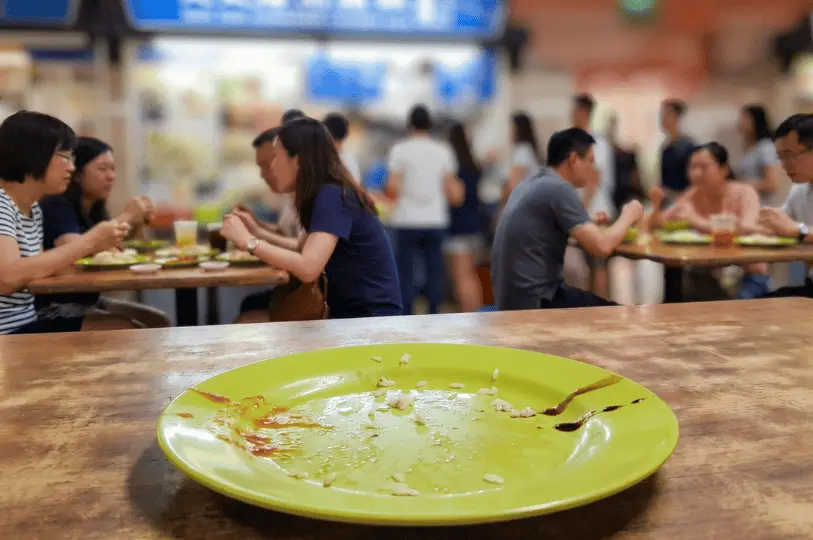 An empty green plate with only smears of sauce and a few stray grains of rice remaining, showing a completely finished meal against the blurred backdrop of a lively dining area.